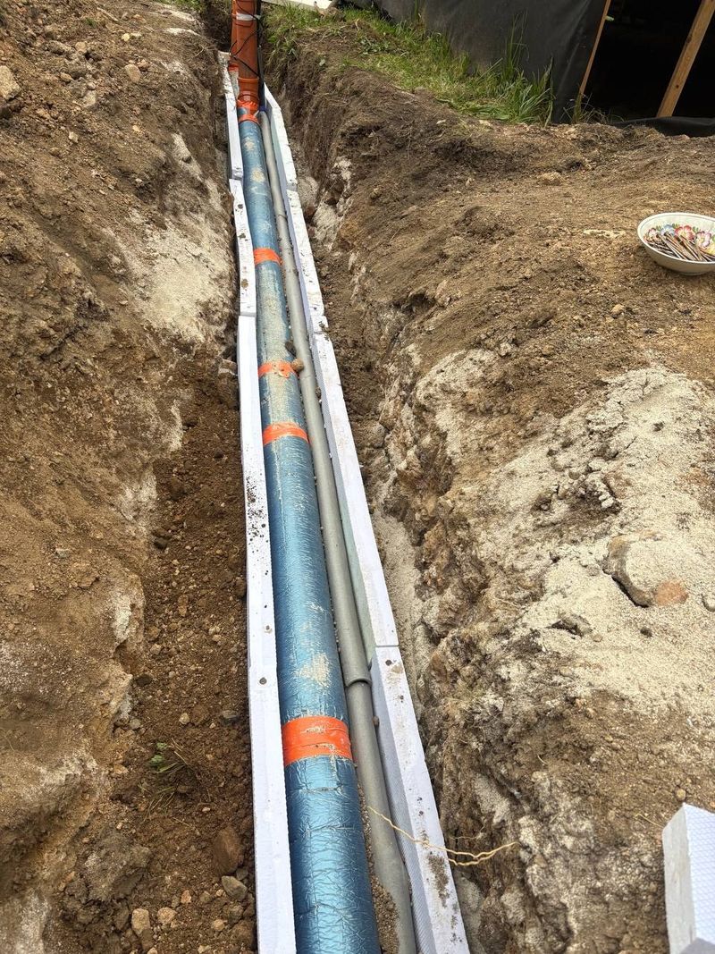 Potrubí v rýze obložené bílými izolačními deskami, oranžové pásky na modré trubce