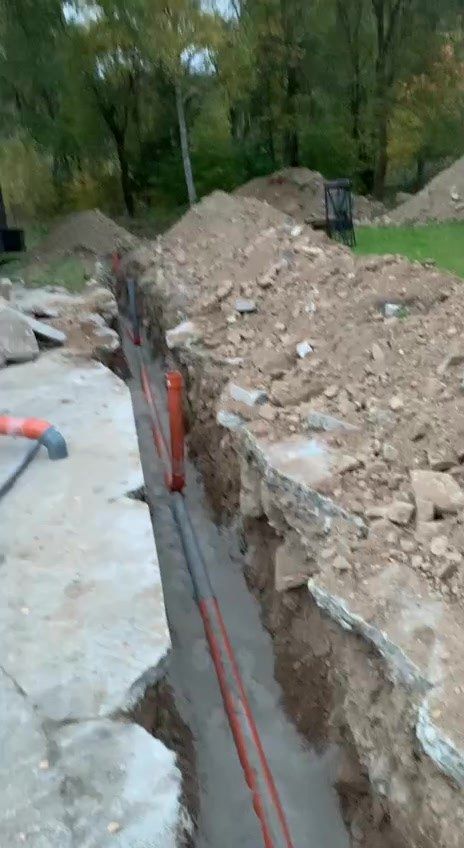 Rýha vybouraná do betonové plochy, v ní oranžové kanalizační trubky