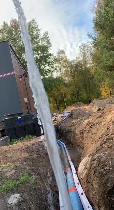 Proud vody z konce potrubí v rýze při zkoušce, v pozadí tmavé domky a stromy